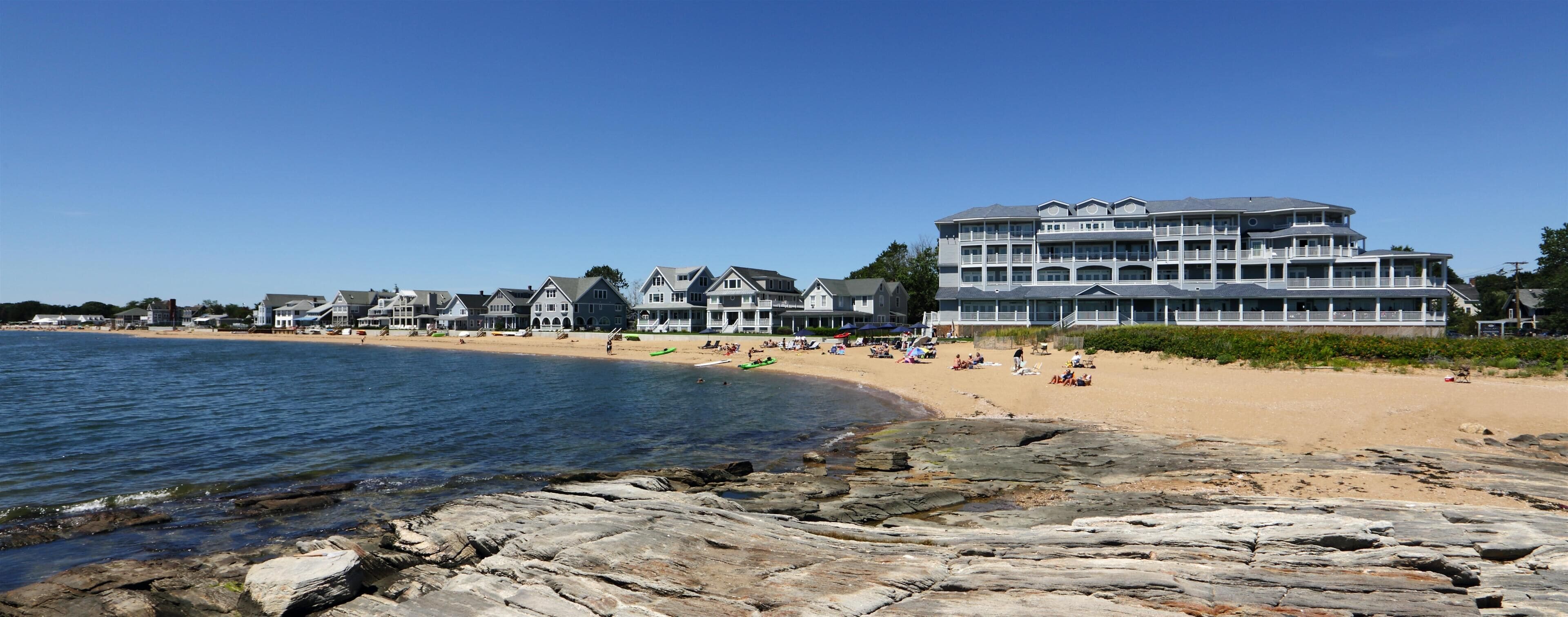 A coastal hotel with multiple balconies, a sandy beach, and a rocky shoreline.