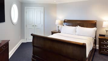 A hotel room with a wooden bed, a nightstand with a lamp, a dresser, a TV, and a door with a window.
