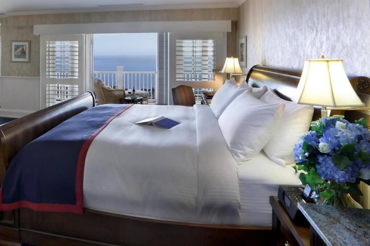 A hotel room with a large bed, a view of the ocean, a desk with a lamp, and a chair.
