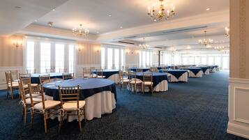 A large banquet hall with round tables, chairs, and chandeliers.