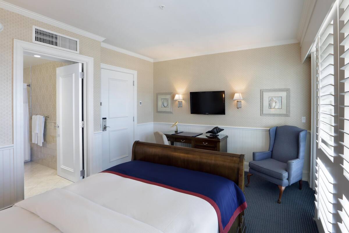 A hotel room with a bed, a desk, a chair, a television, and a window with blinds.