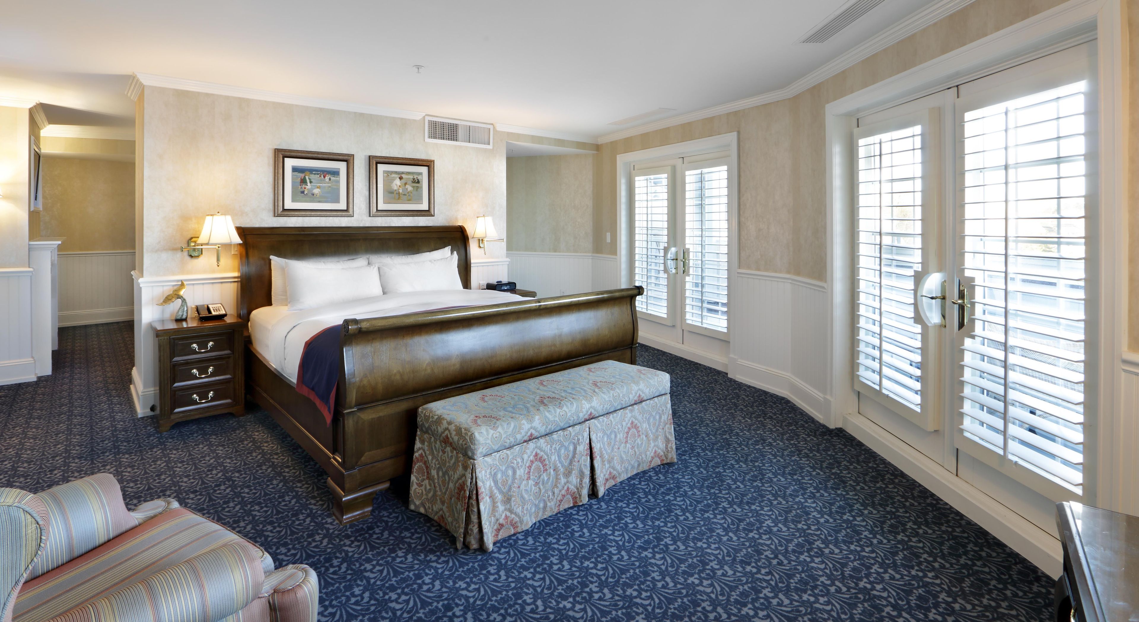 A hotel room with a large bed, a bedside table, a lamp, a chair, and a window with blinds.