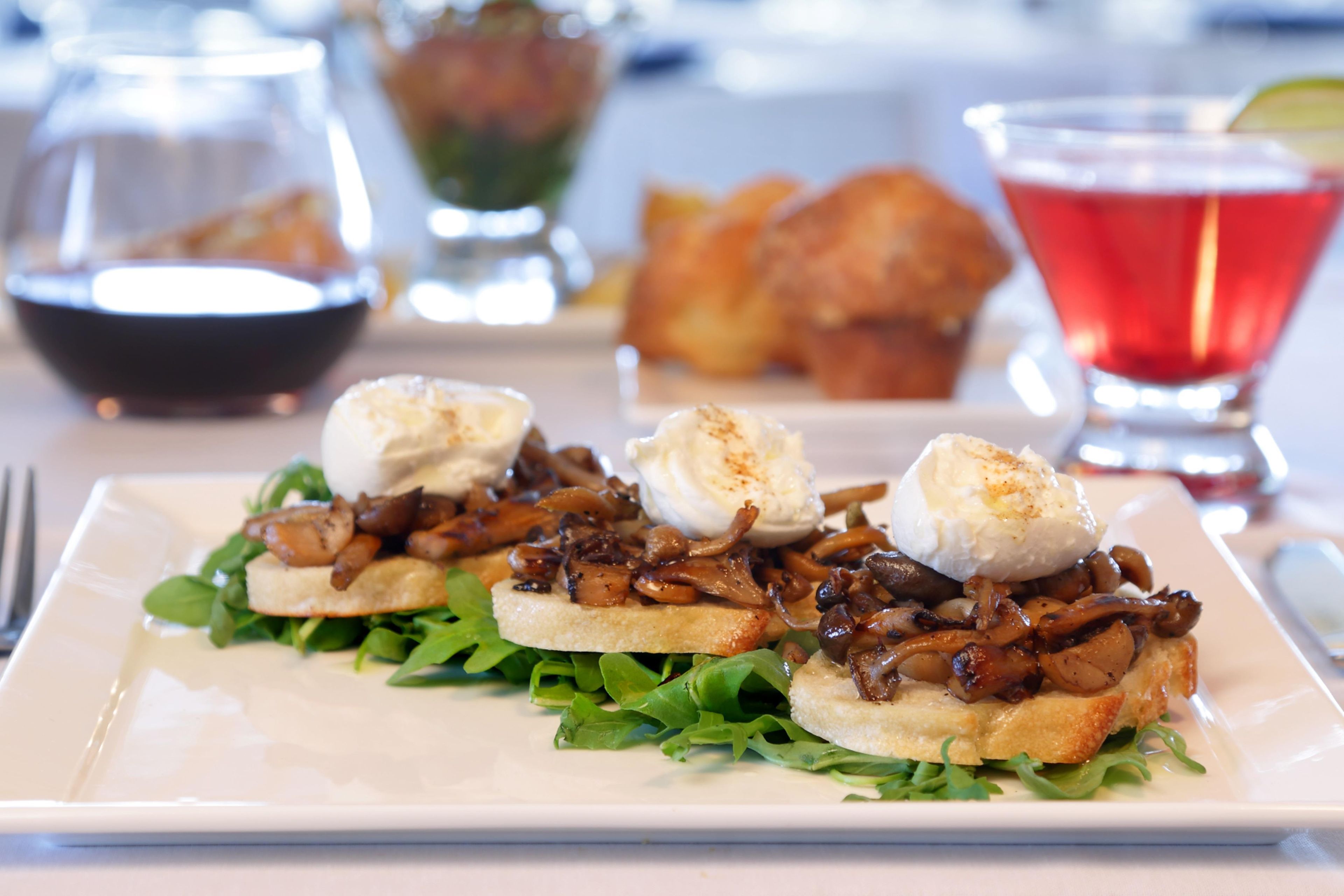 A plate of food with mushrooms and poached eggs on toast, accompanied by a glass of red drink and a bowl of soup.
