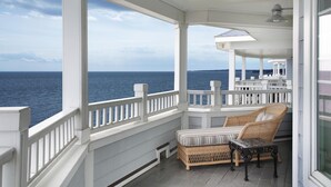 A covered porch with a view of the ocean, a wicker chair, and a small table. - Madison Beach Hotel (Madison)