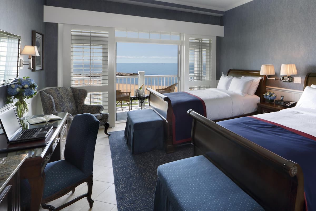 A hotel room with a large bed, two bedside tables, a desk with a laptop, a chair, and a balcony with a view.