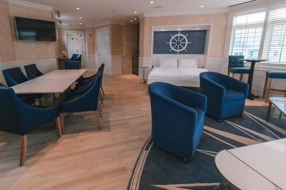 A hotel room with a dining area, a bed, a TV, and a sail wheel decoration.