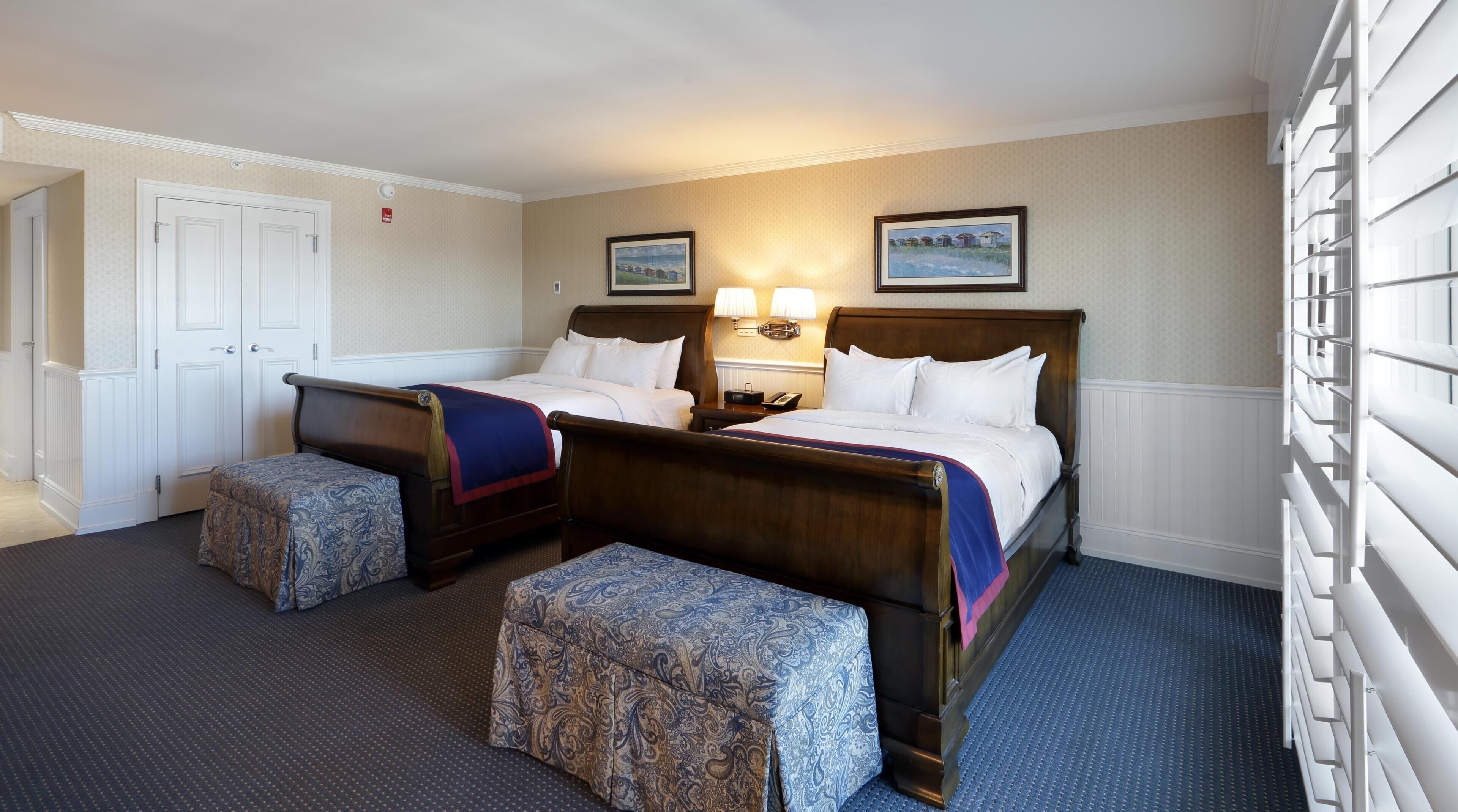 A hotel room with two beds, a desk, two bedside tables, a chair, and a wardrobe.