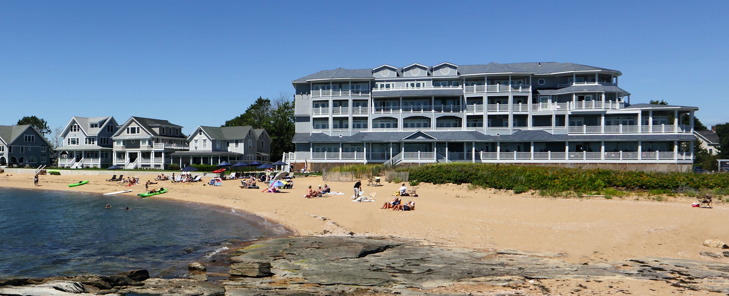 A beachfront hotel with multiple balconies, a sandy beach, and a rocky shoreline.