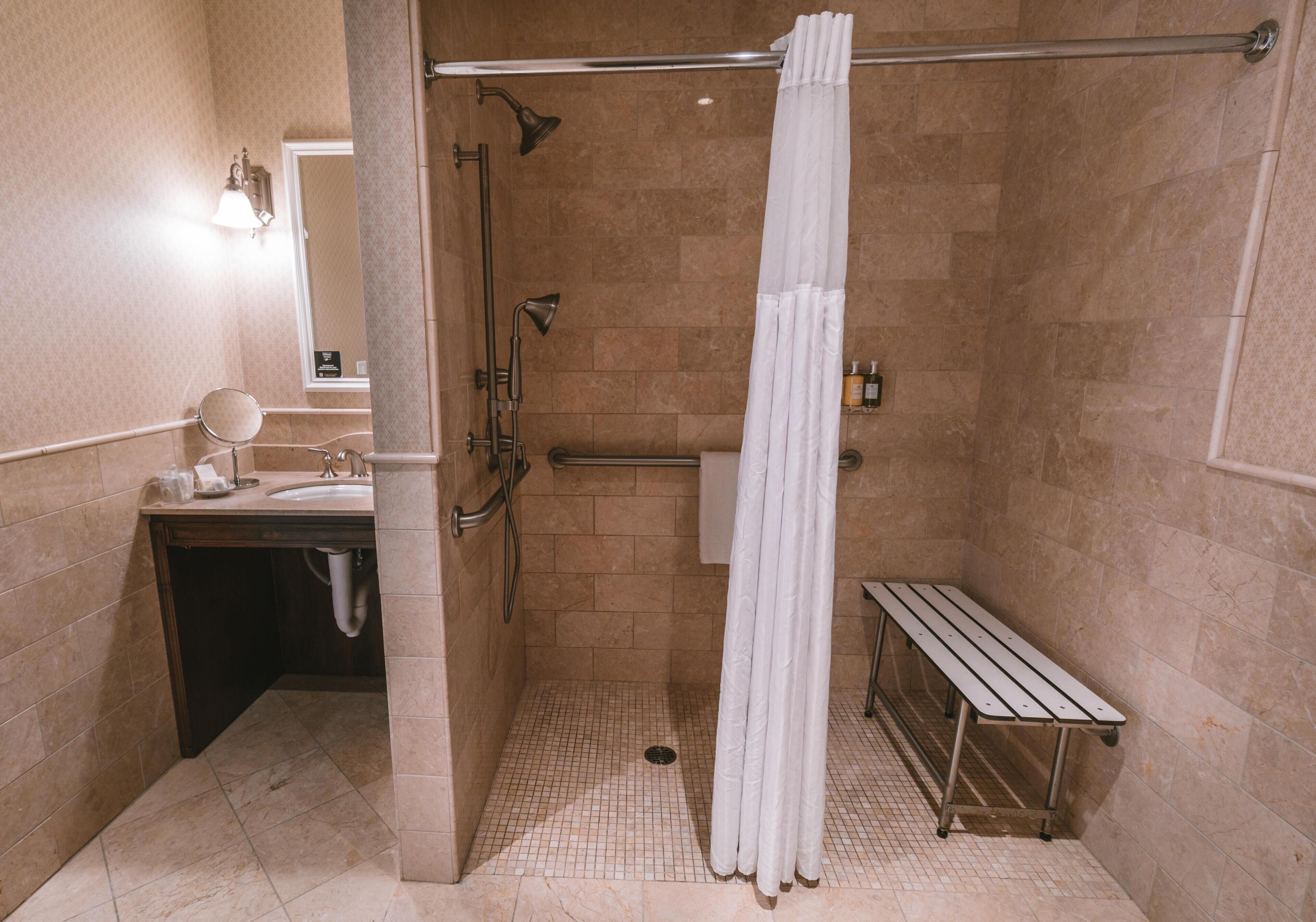 A bathroom with a shower, a bench, a sink, and a mirror.