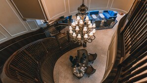 A grand spiral staircase with a chandelier, a round table with chairs, and a blue sofa in a spacious lobby area. - Madison Beach Hotel (Madison)
