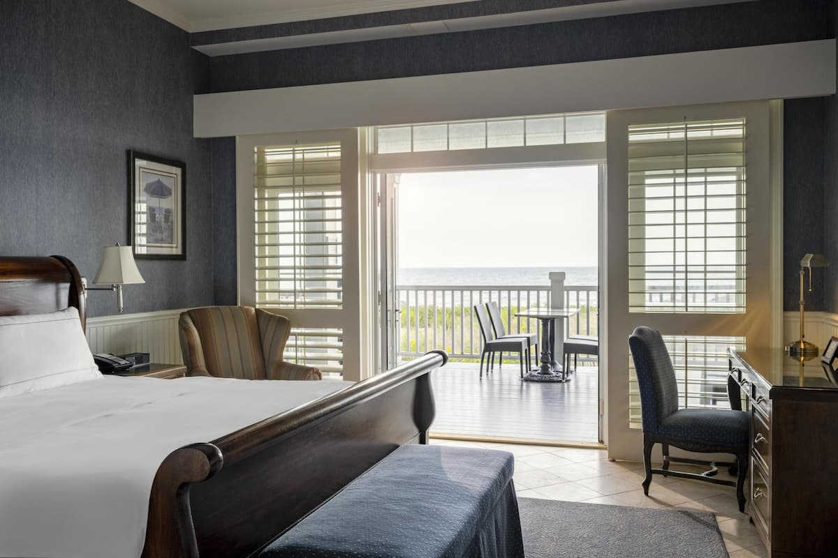 A hotel room with a bed, a desk, a chair, and a balcony with a view of the sea.