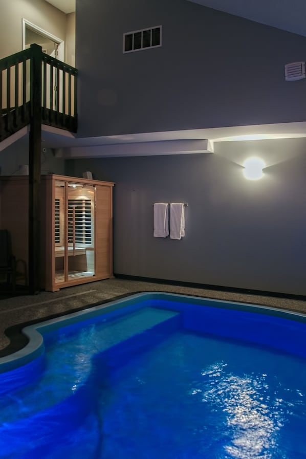 A swimming pool with a wooden deck, a glass door leading to a room, and a light fixture on the wall. - Belamere Suites Hotel (Perrysburg)