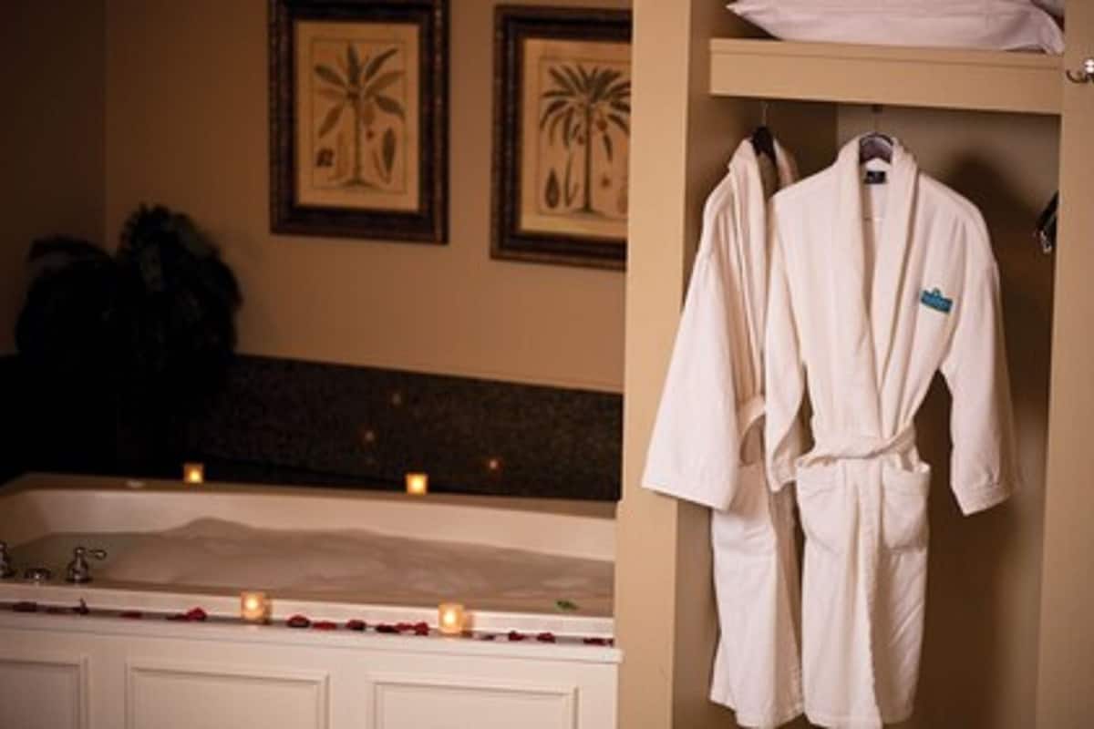 Ein Badezimmer mit einer Badewanne, zwei gerahmten Bildern von Palmen und einem Bademantel auf einem Haken.