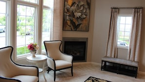Un salon avec une cheminée, deux fauteuils, une petite table sur laquelle est posé un vase de fleurs et un banc.