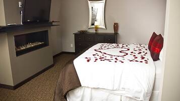 A hotel room with a bed, a dresser, a television, and a fireplace.