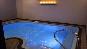 A hot tub with a metal ladder, a wall-mounted light fixture, and a small white object on the wall.