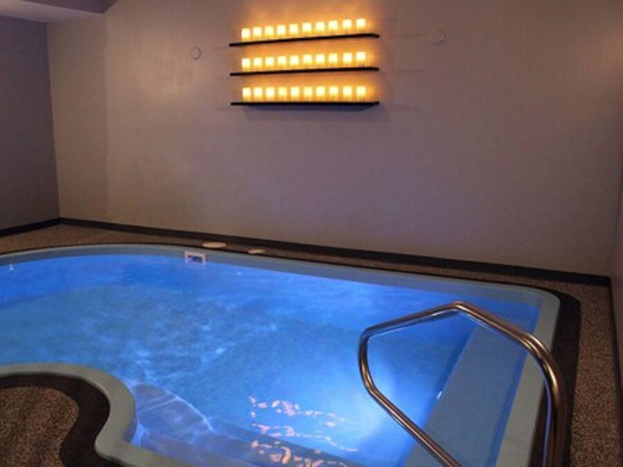 A hot tub with a metal ladder, a wall-mounted light fixture, and a small white object on the wall.
