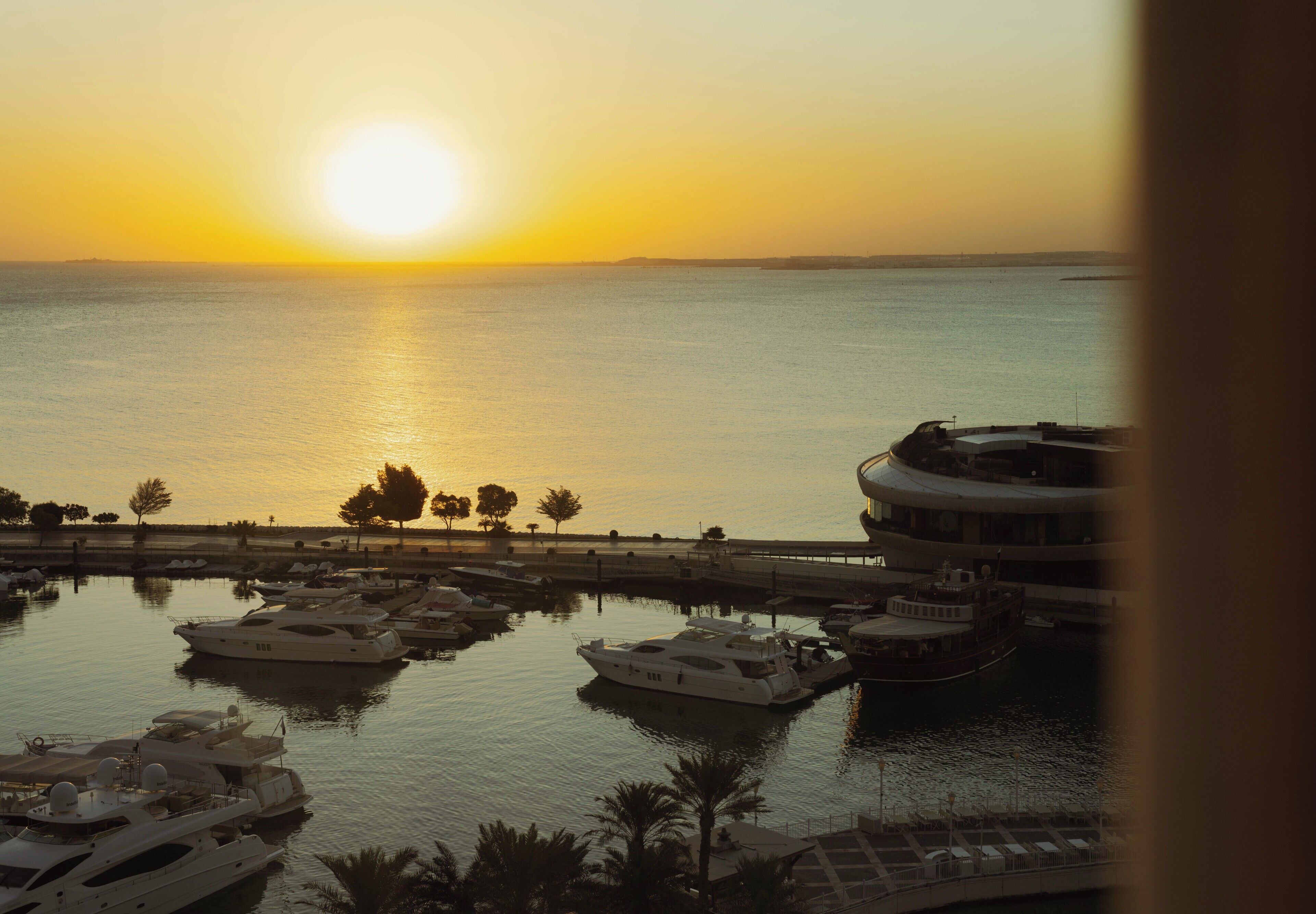 Un port de plaisance avec des bateaux amarrés, une promenade en bord de mer et un coucher de soleil en arrière-plan.