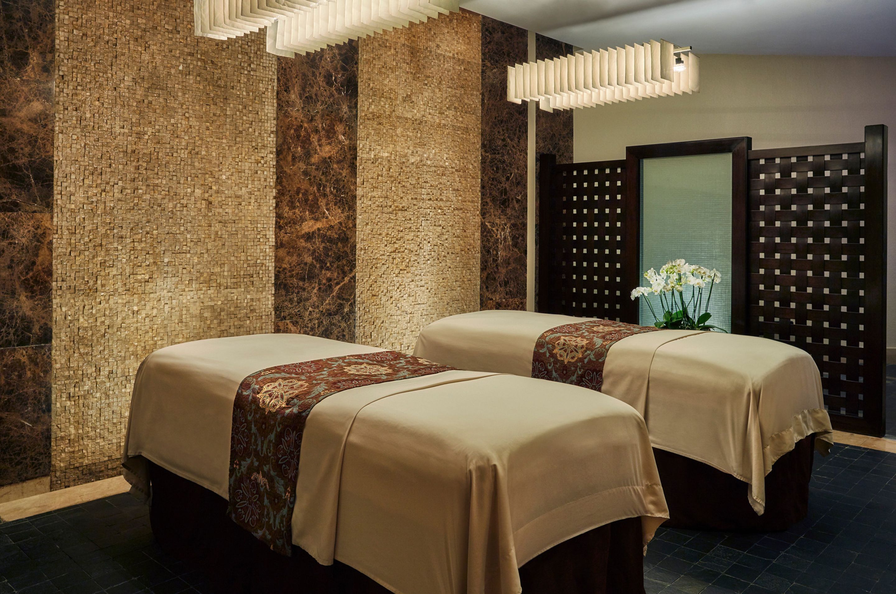 A spa room with two massage tables, a decorative wall, and a modern light fixture.