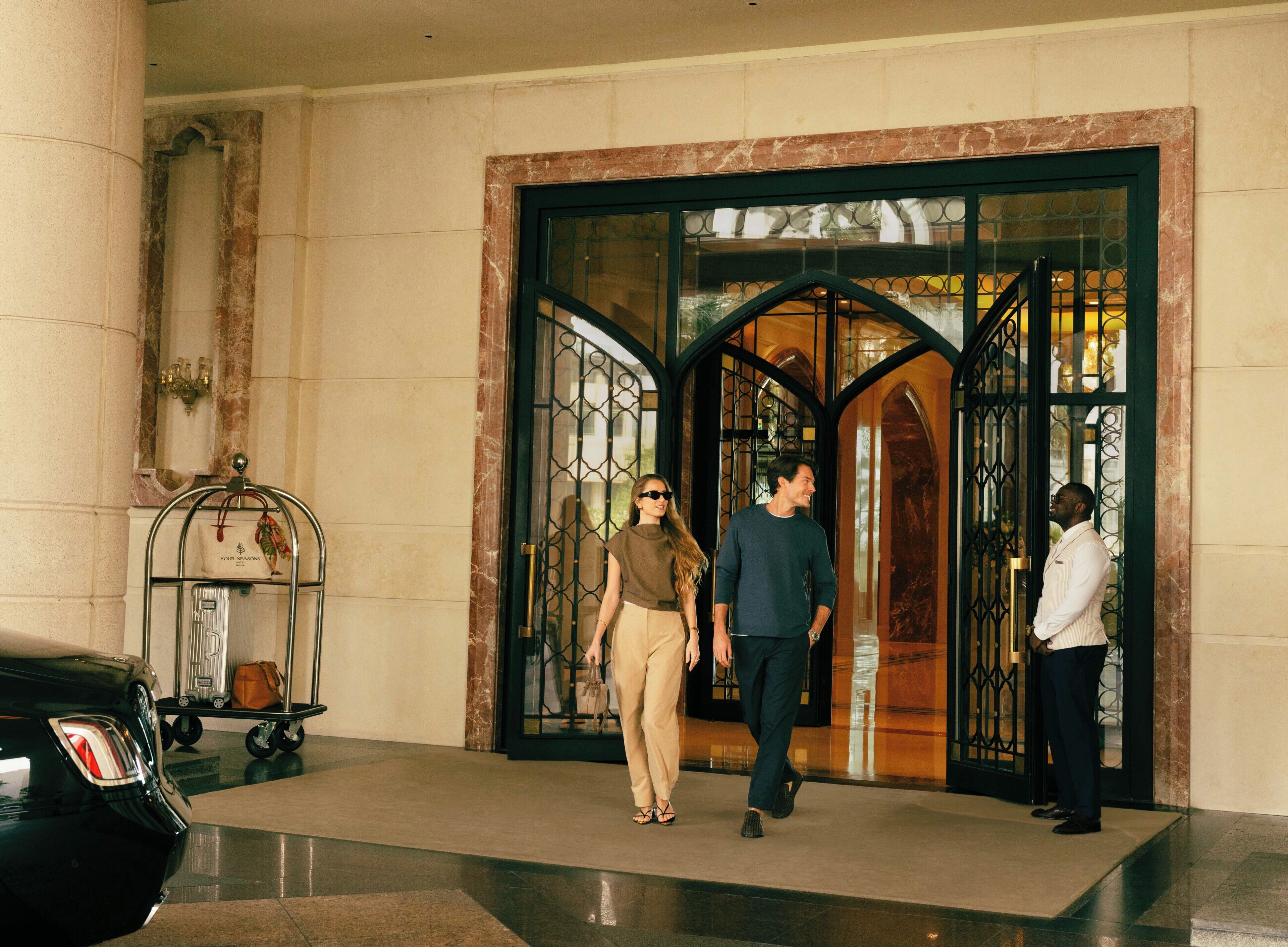 Entrada de hotel con una columna de mármol, una reja metálica y un carrito de equipaje.