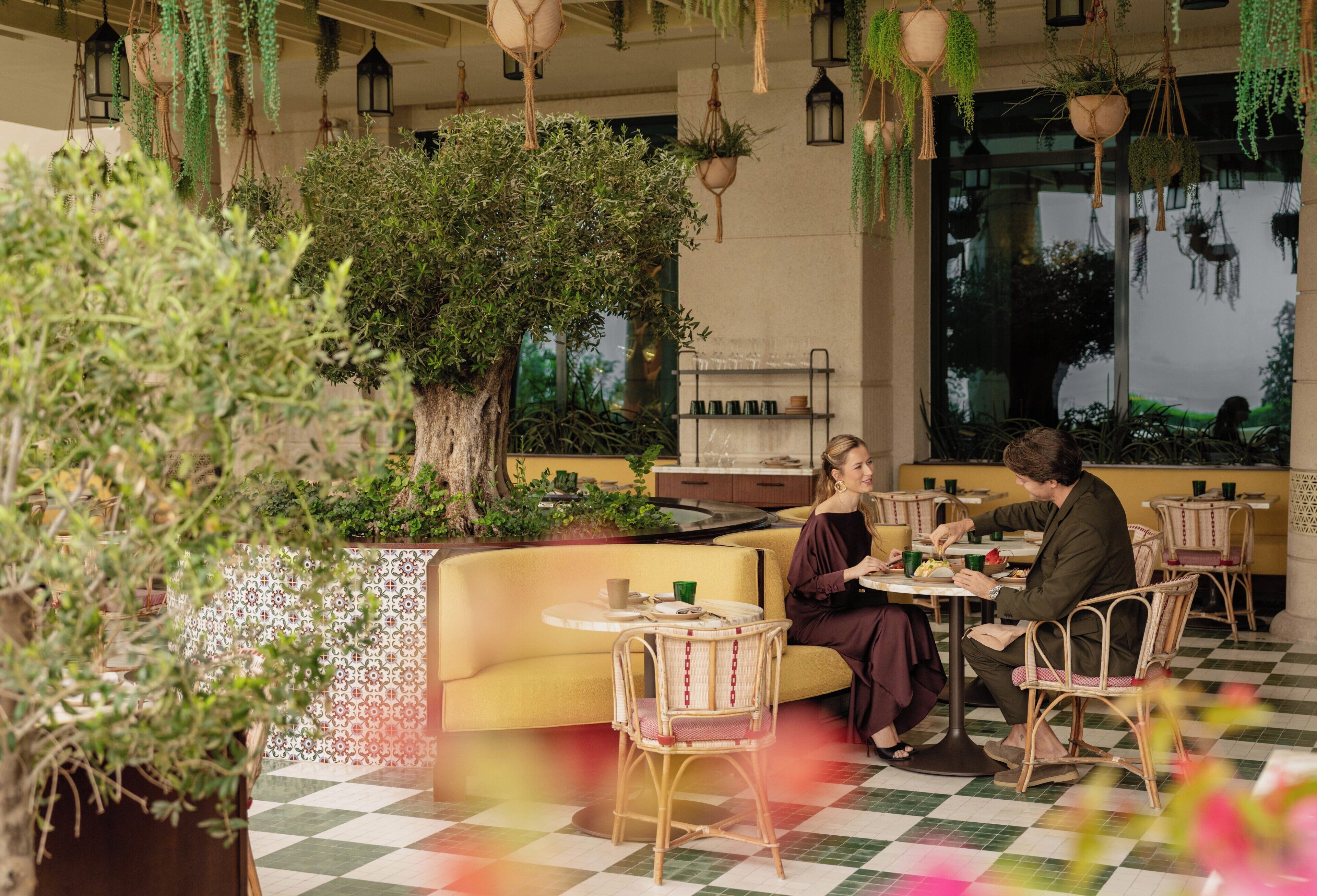 Un restaurant doté d’une terrasse, d’un grand arbre, de plantes suspendues et de chaises en osier.