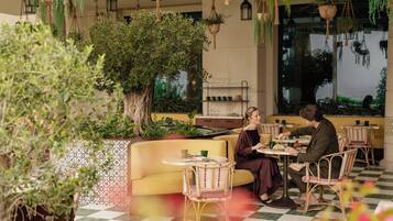 Un restaurant doté d’une terrasse, d’un grand arbre, de plantes suspendues et de chaises en osier.