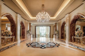 A grand lobby with a chandelier, marble columns, and a geometric floor design.