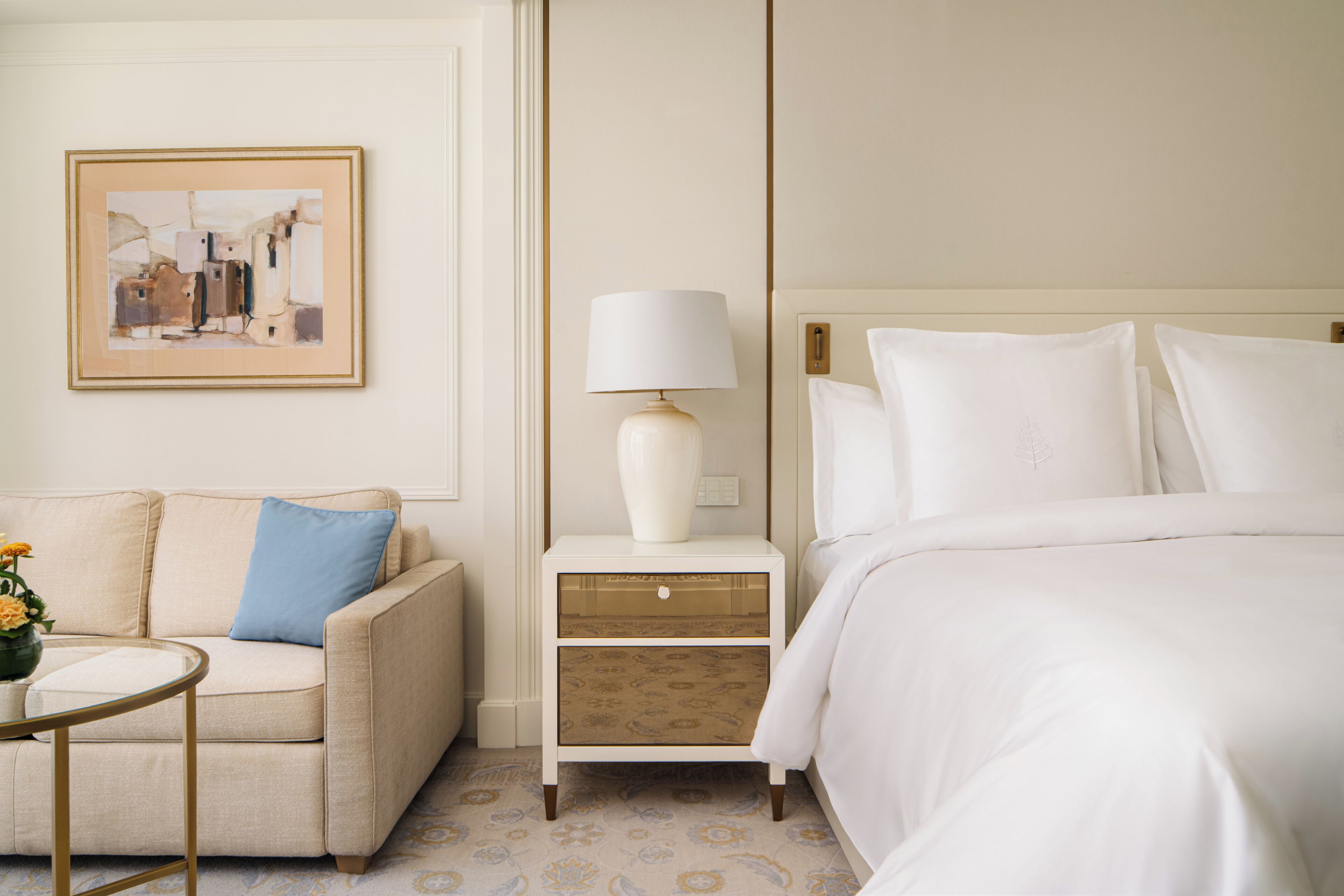 A hotel room with a bed, a nightstand with a lamp, a sofa, and a framed picture on the wall.