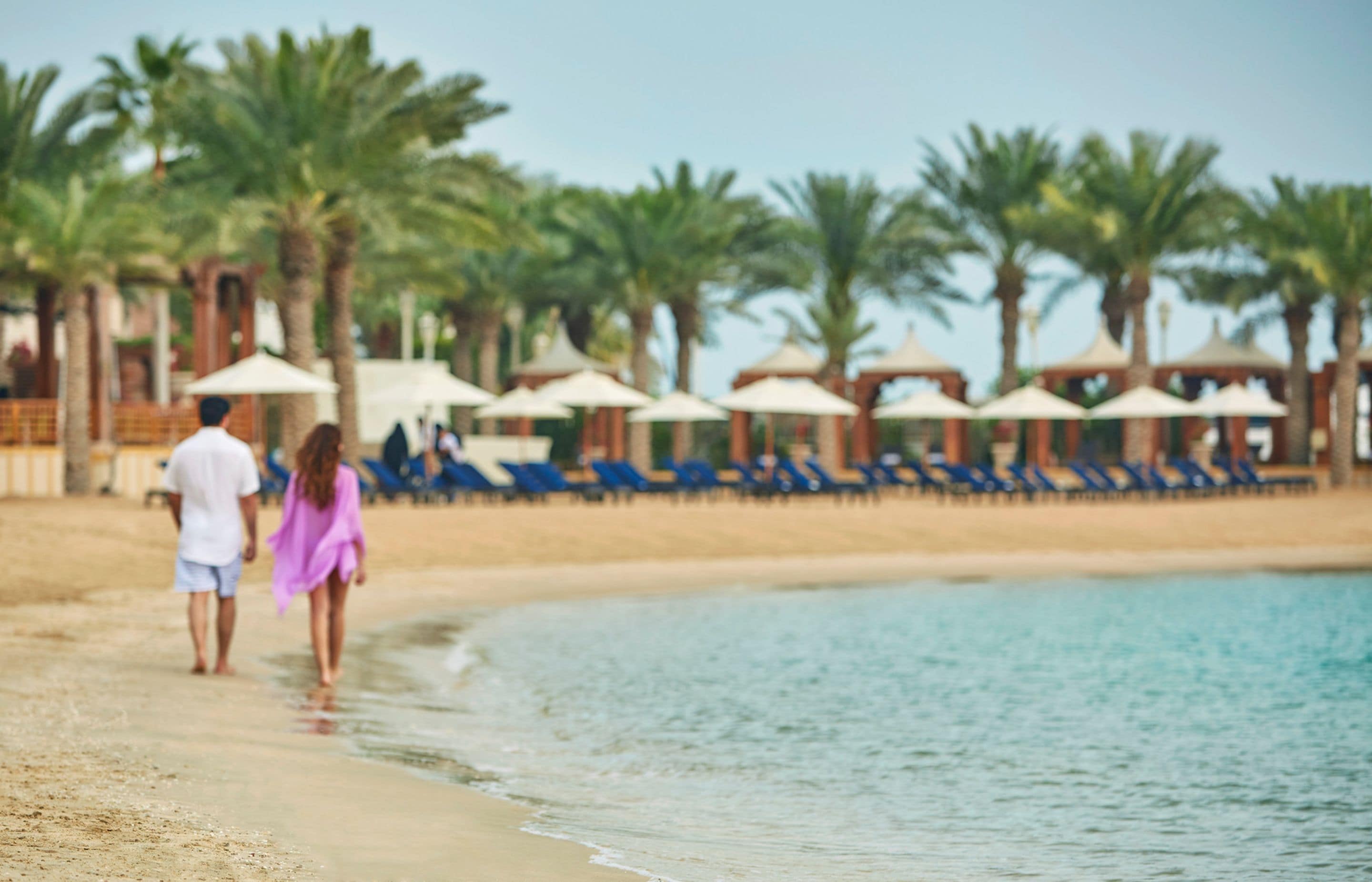 A beach with palm trees and lounge chairs.