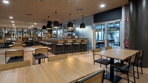 Um café moderno com mesas e cadeiras de madeira, um balcão e grandes janelas.