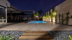 Uma área de piscina com deck de madeira, borda de pedra e área de estar coberta.