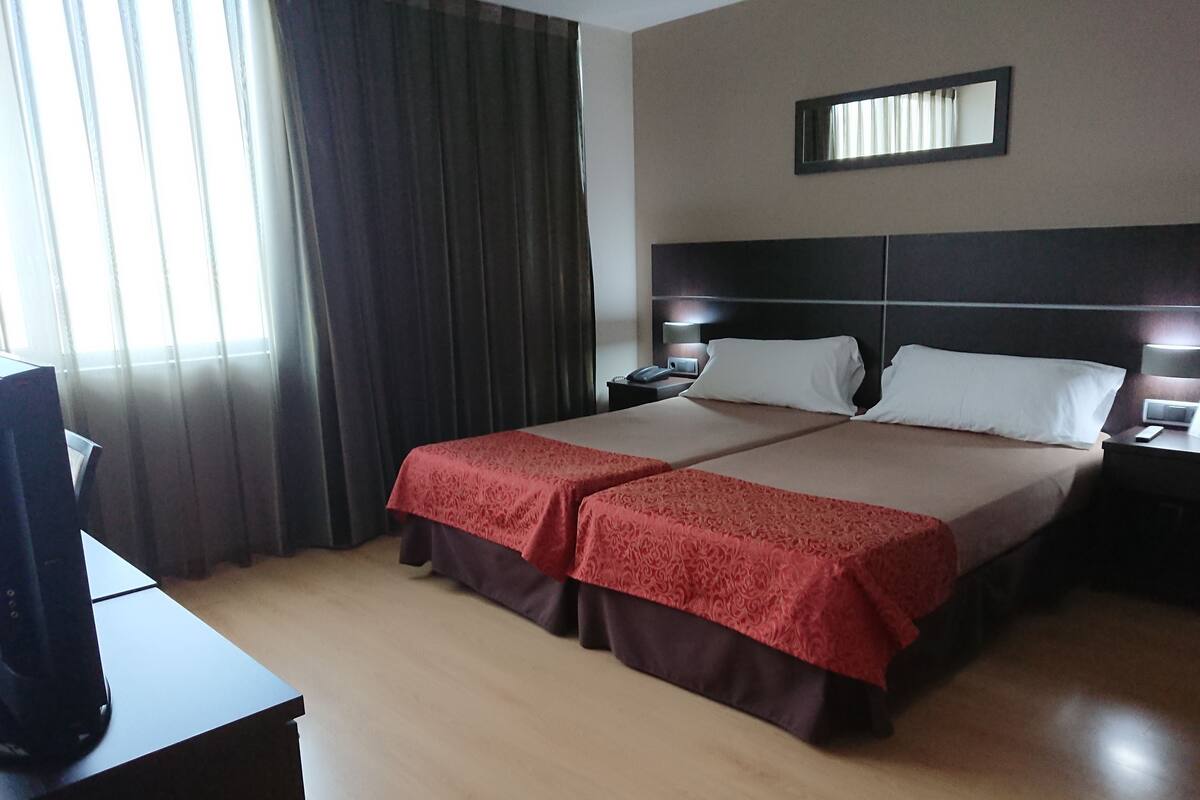 A hotel room with a large bed, a bedside table, a TV, and a window with curtains.