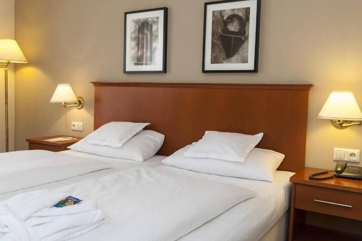A double bed with white linens, two bedside tables with lamps, and two framed pictures on the wall.