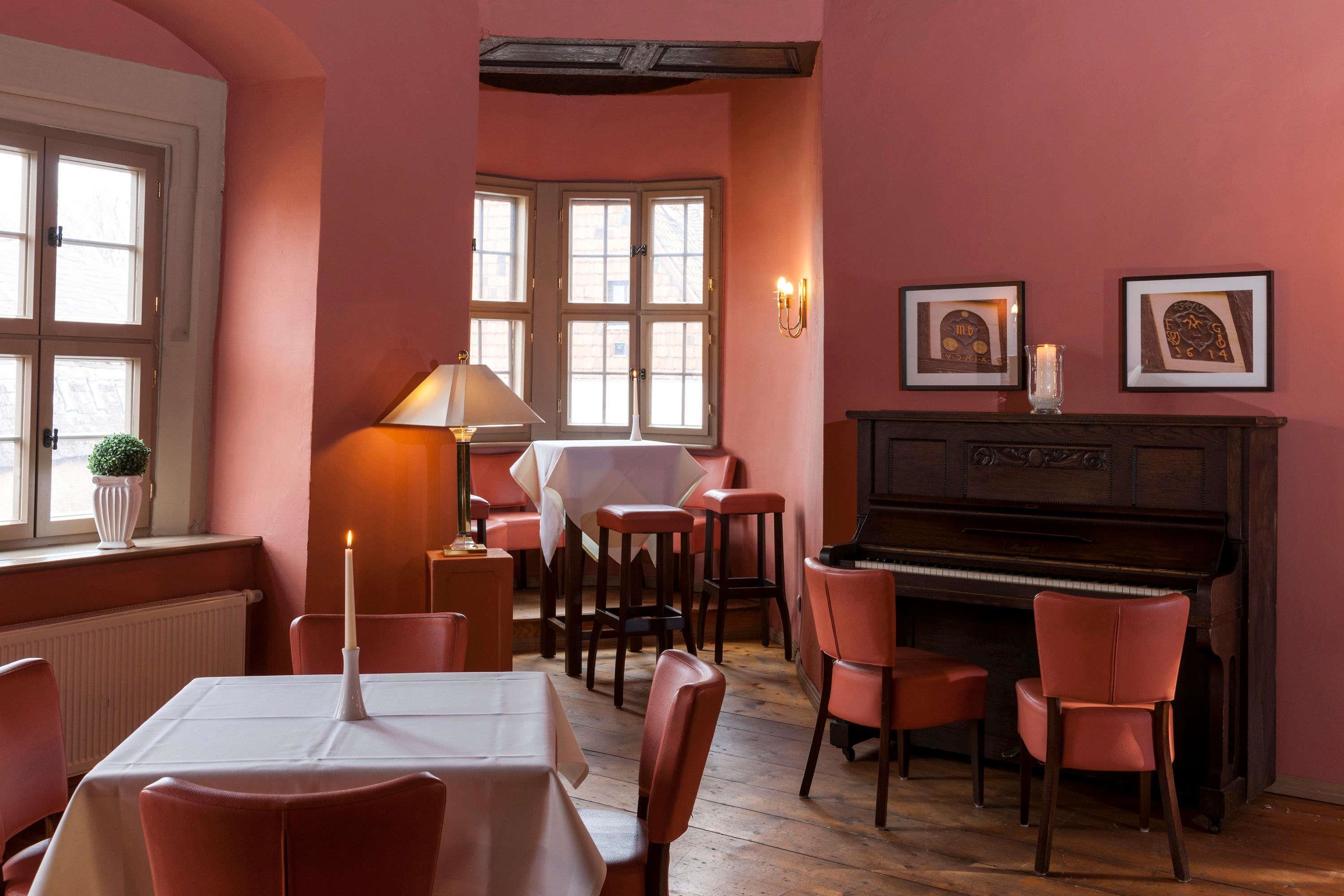 Un comedor con un piano, sillas rojas, una mesa con una vela y cuadros en la pared.