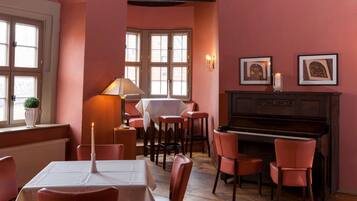 Un comedor con un piano, sillas rojas, una mesa con una vela y cuadros en la pared.