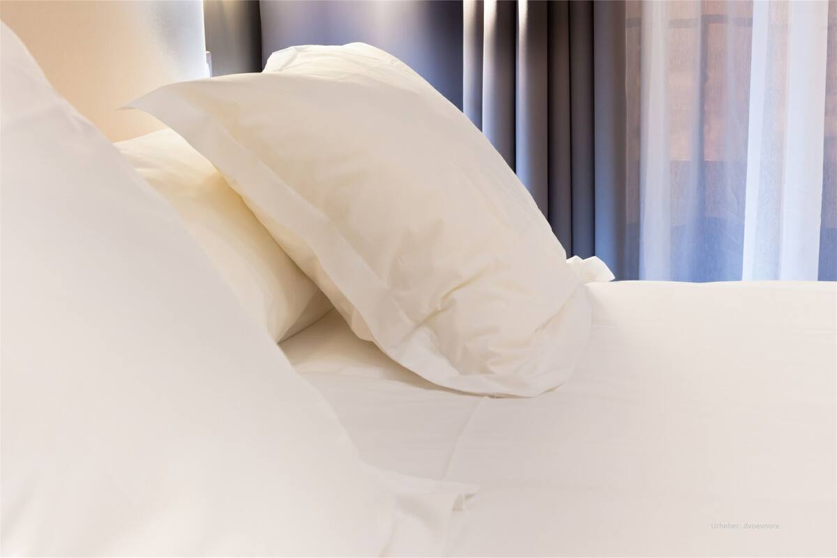 A neatly made bed with white bedding and pillows.