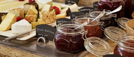 A variety of cheeses and jams on a buffet table with labels.