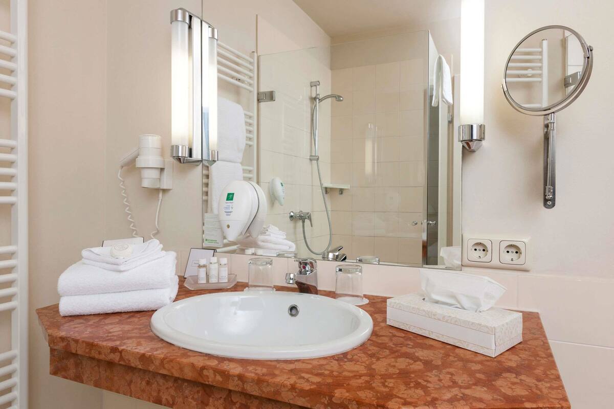 A bathroom with a sink, towel dispenser, hairdryer, and a mirror.