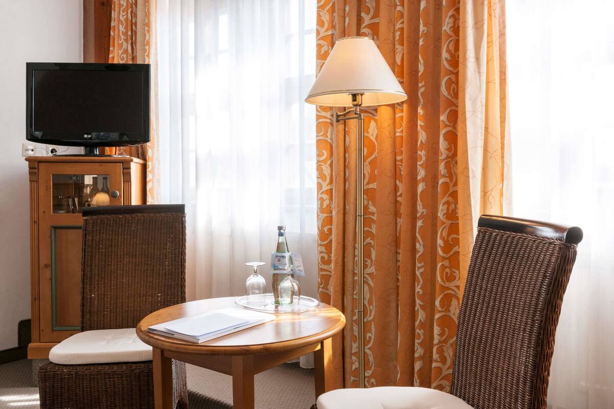 A hotel room with a television, a table with a lamp, wicker chairs, and a bottle of water.