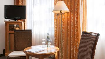 Una habitación de hotel con televisión, una mesa con lámpara, sillas de mimbre y una botella de agua.