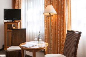 Una habitación de hotel con televisión, una mesa con lámpara, sillas de mimbre y una botella de agua.