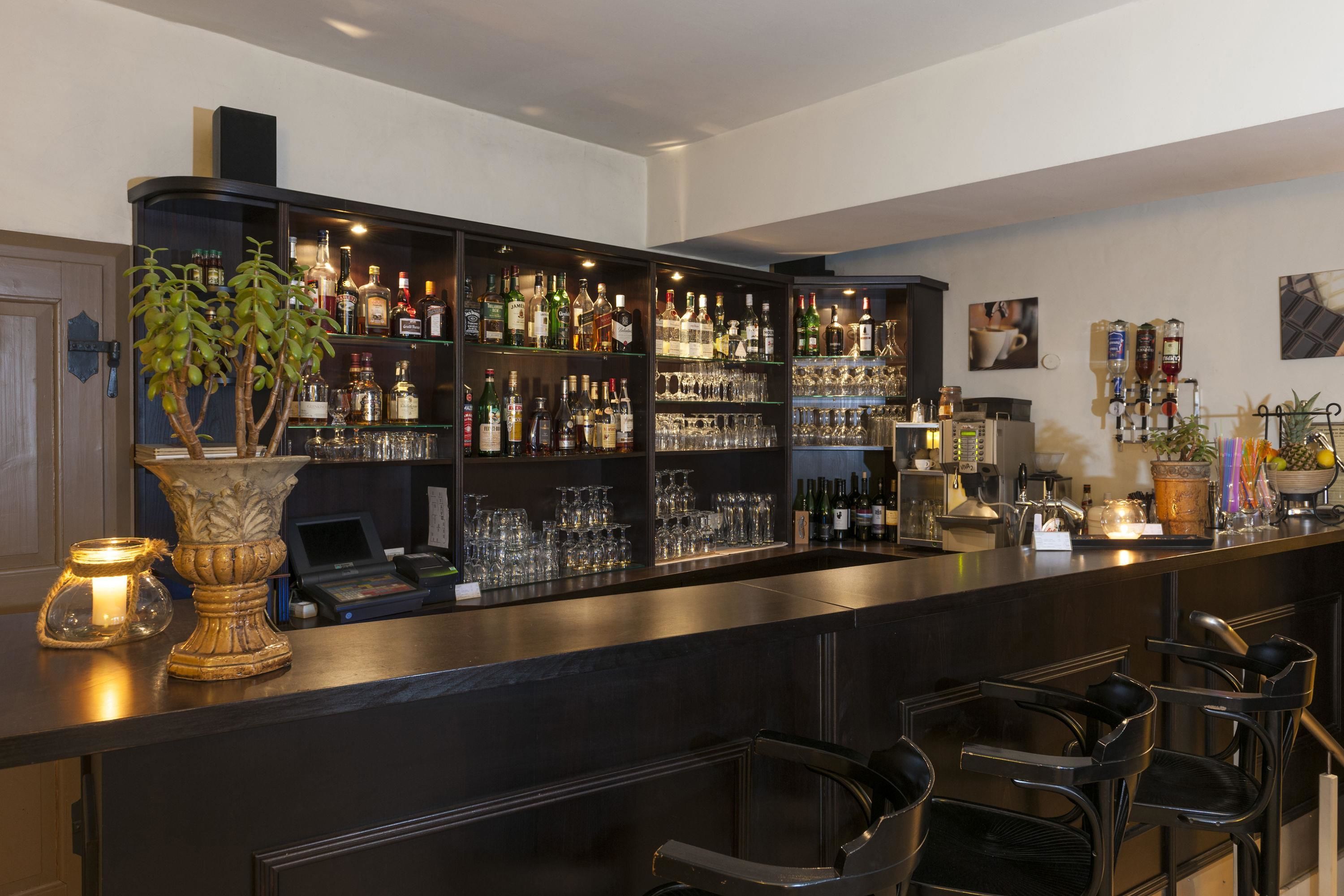 Un espace bar avec des étagères remplies de bouteilles d’alcool, des verres et un ordinateur portable posé sur le comptoir.