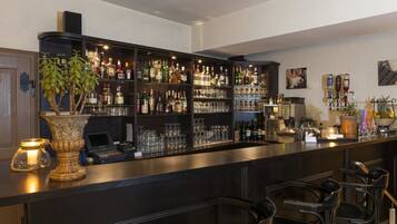 Una zona de bar con estantes llenos de botellas de licor, vasos y un ordenador portátil sobre la barra.