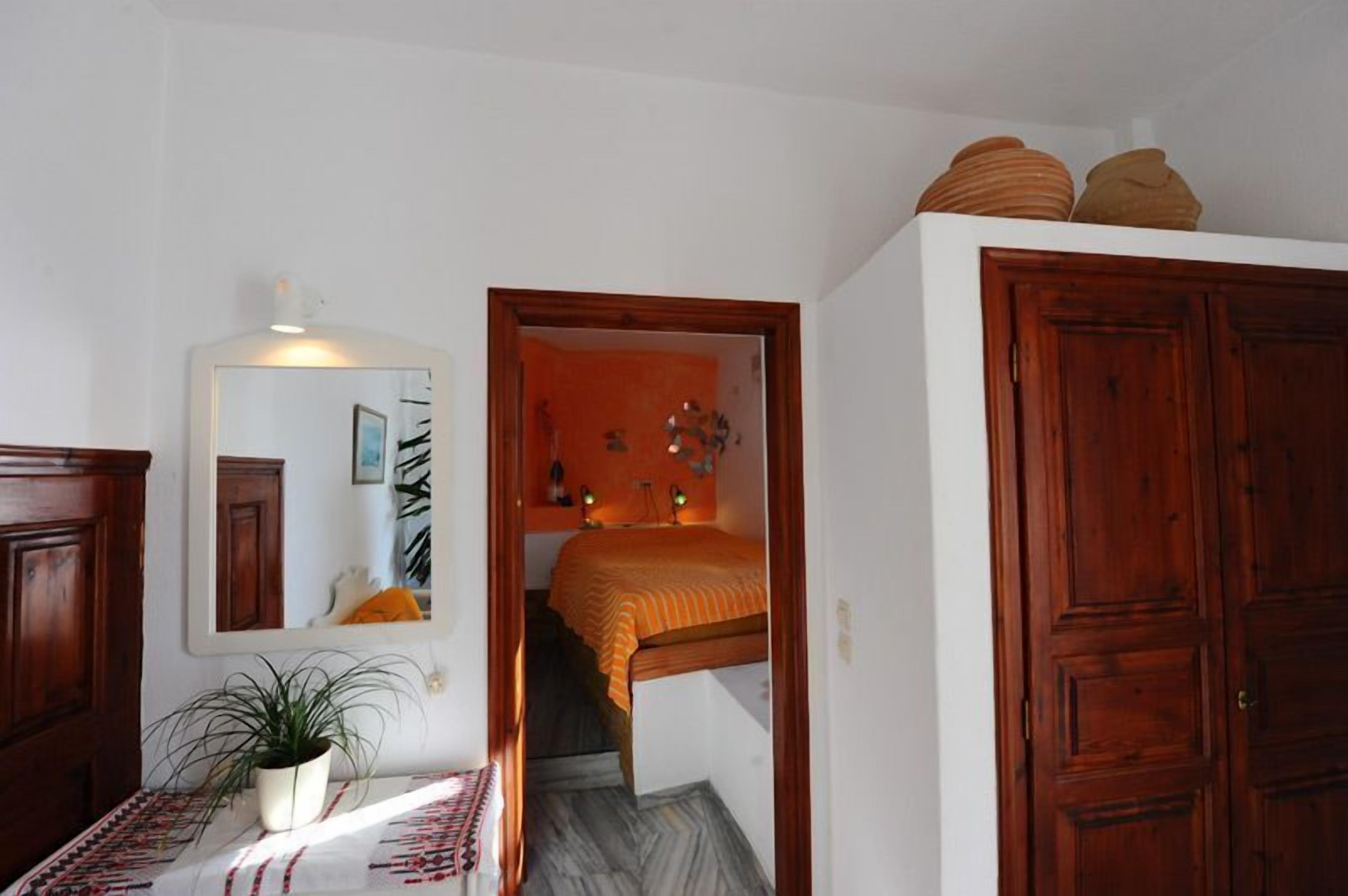 A bedroom with a bed, a wooden wardrobe, a mirror, and a potted plant.