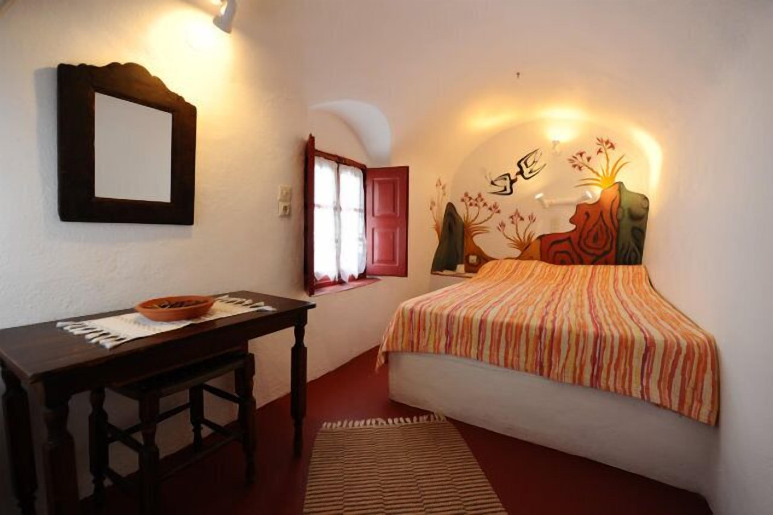 Un dormitorio con cama, mesita de noche, espejo y lámpara de pared.