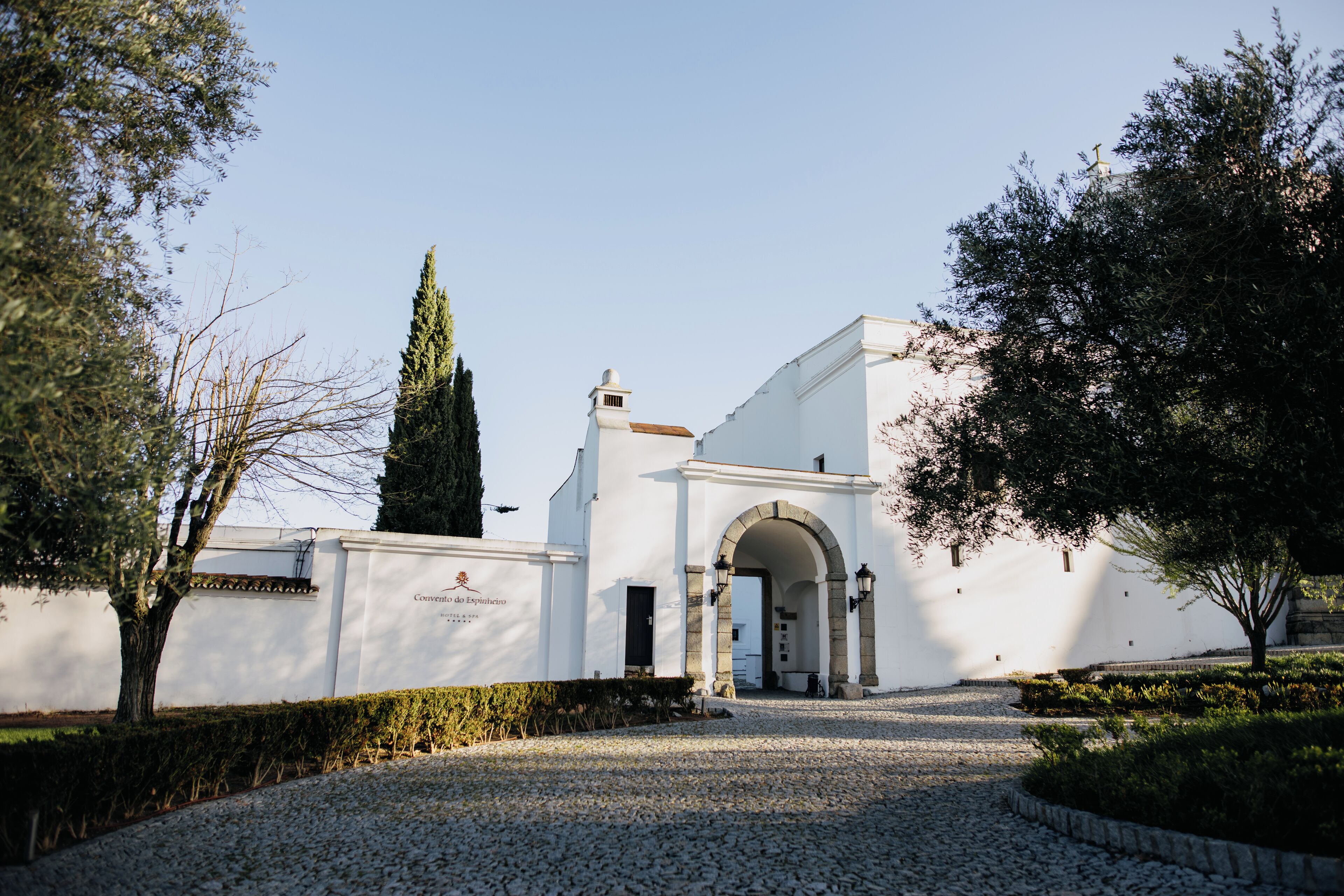 Um edifício com fachada branca, entrada em arco e um caminho de cascalho que leva até ele.