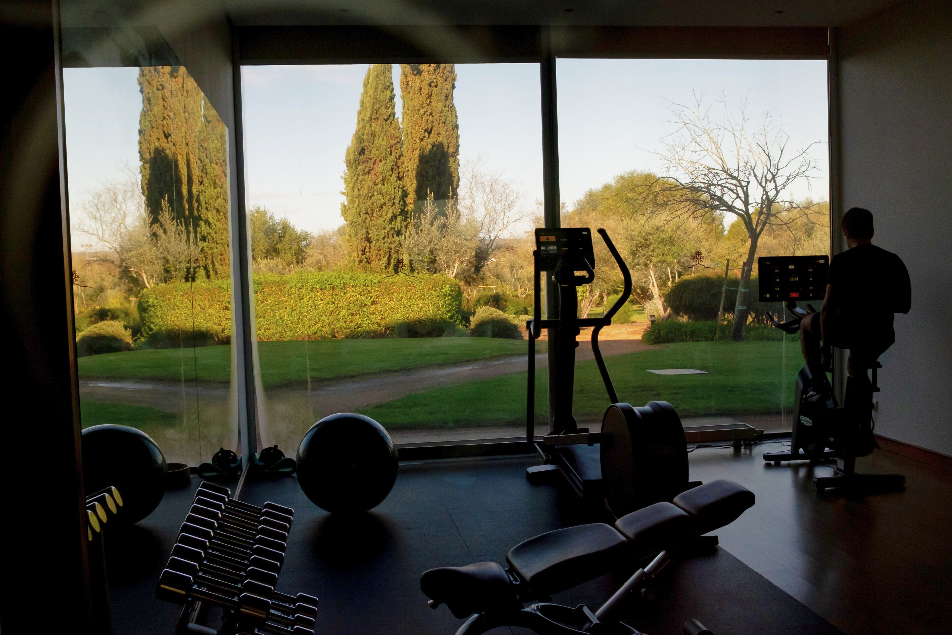 A gym with exercise equipment, a large window with a view of a golf course, and a person using a stationary bike.
