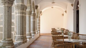 A dining area with stone columns, wicker chairs, and a tiled floor. - Convento do Espinheiro, Historic Hotel & Spa (Évora)