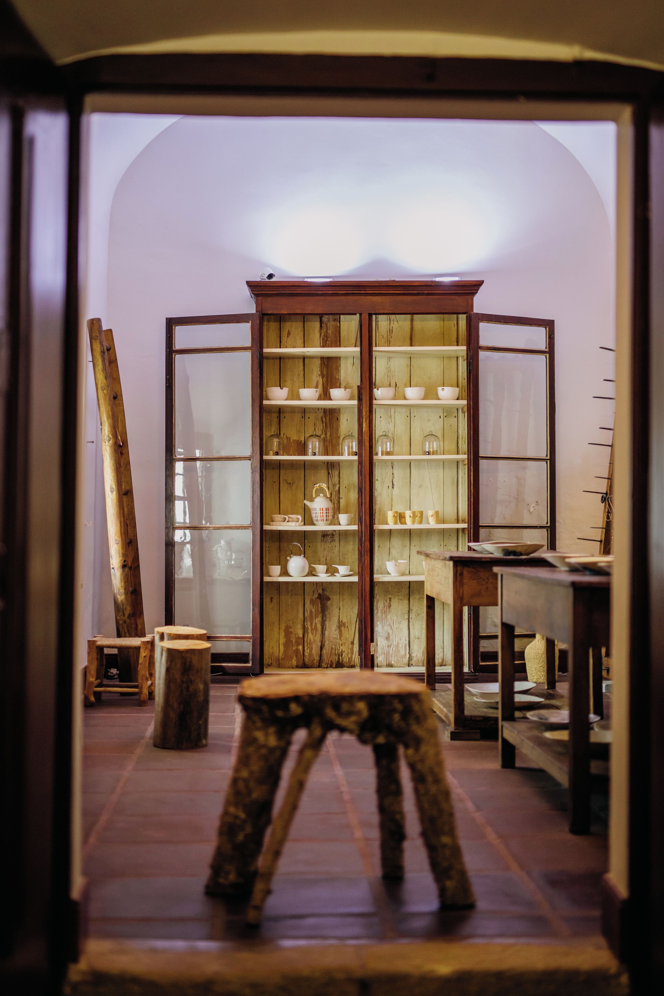 A room with a wooden cabinet filled with dishes, a ladder, and a stool.