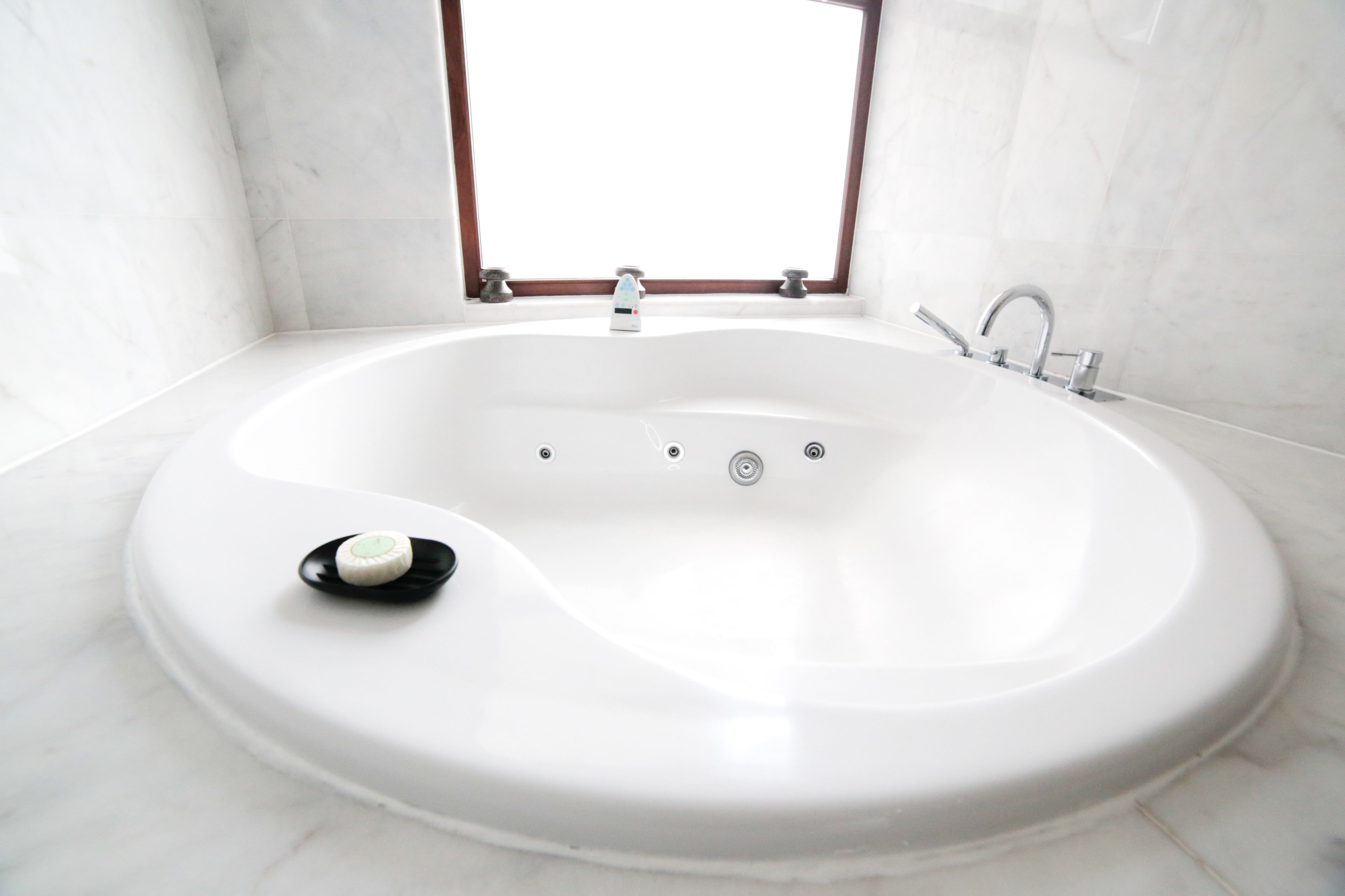 A modern bathroom with a freestanding bathtub, a window above the tub, and a marble floor.